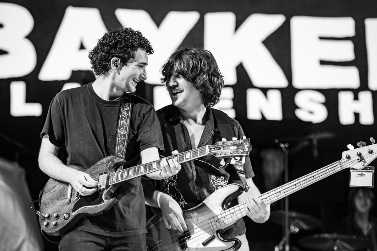 Two guitarists leaning together and laughing on stage, in black and white