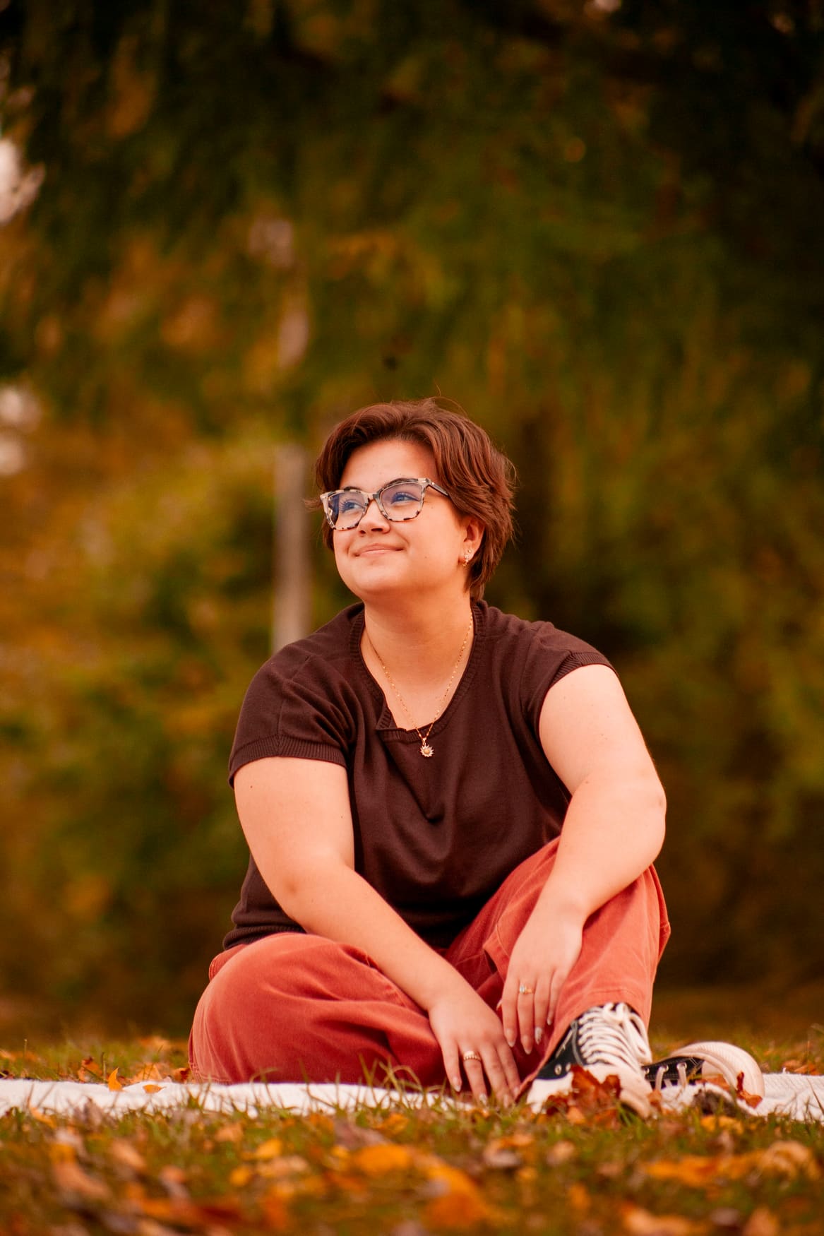 Senior portrait of a person seated on a blanket among autumn leaves