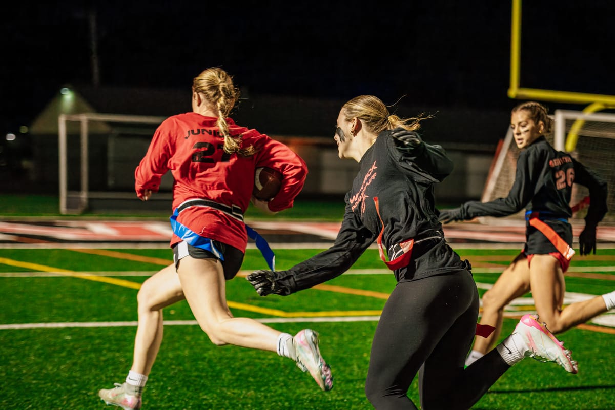Flag football players chasing down the ball carrier under stadium lights
