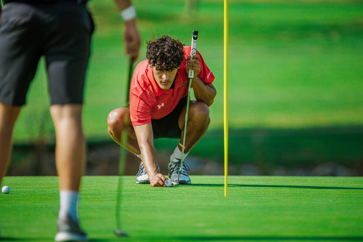 Golfer crouched to set the tee marker on the green
