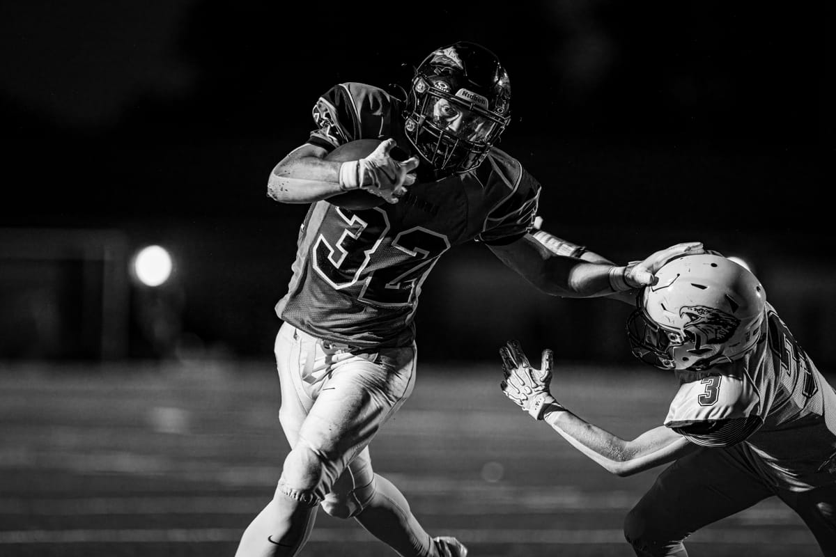 Running back delivering a stiff-arm under the lights, in black and white