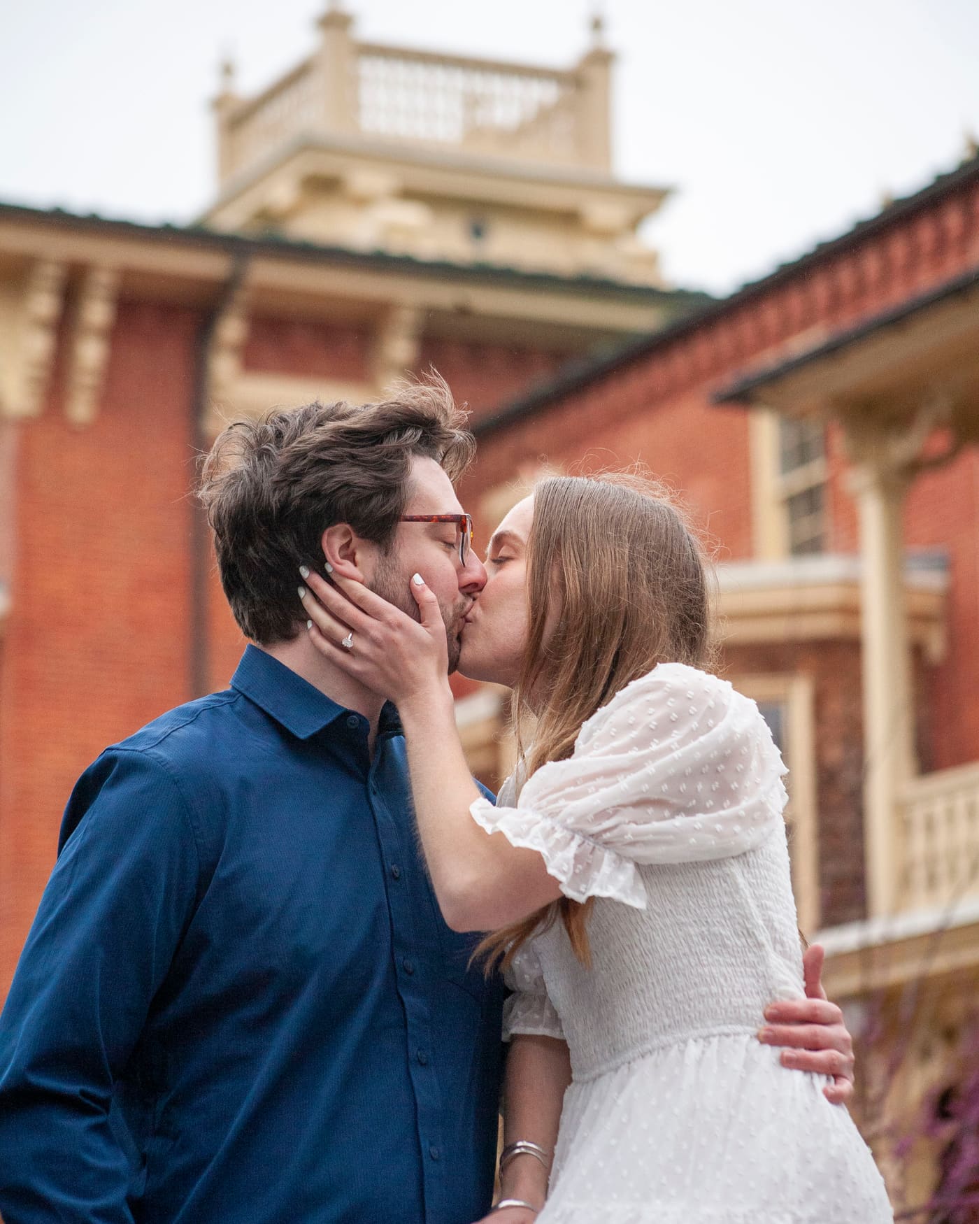 Couple sharing a kiss in a brick courtyard, engagement ring in view