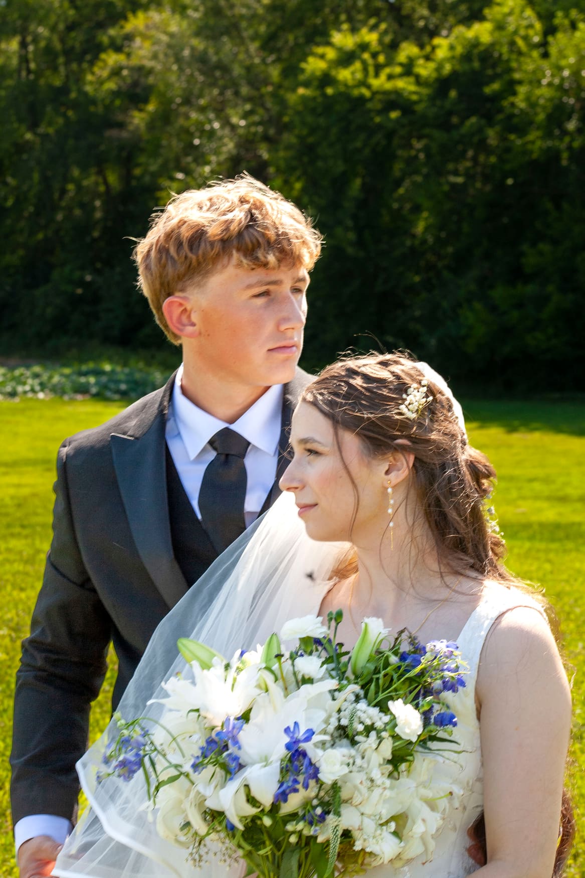 Bride holding a white and blue bouquet with the groom in a sunlit field